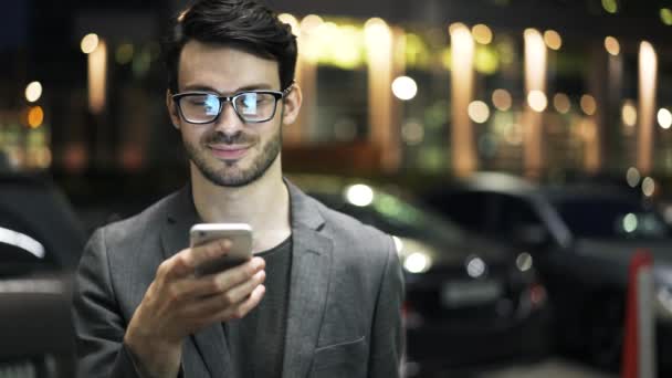 Joven hombre de negocios en gafas navegando por la red exterior y sonriendo — Vídeos de Stock