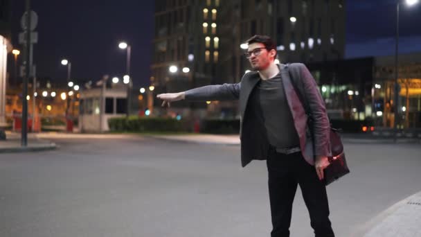 Jovem empresário tentando parar um carro em uma rua noturna — Vídeo de Stock