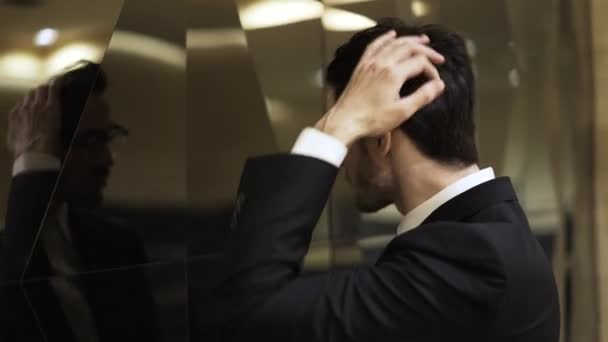 Side view of a handsome businessman brushing his hair with a hand outside — Stock Video