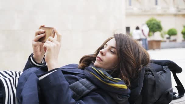Молодая туристка лежит на улице Валенсии и пользуется своим смартфоном — стоковое видео