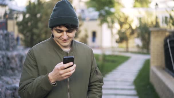 Junge schwarzhaarige Kerl SMS in einem Park — Stockvideo