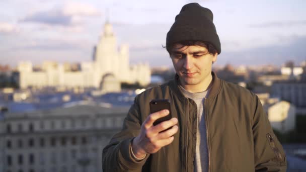 Junger Mann in Mütze textet auf einem Dach — Stockvideo