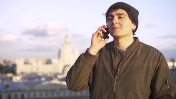 Mann trägt eine Mütze auf einem Handy auf einem Dach — Stockvideo