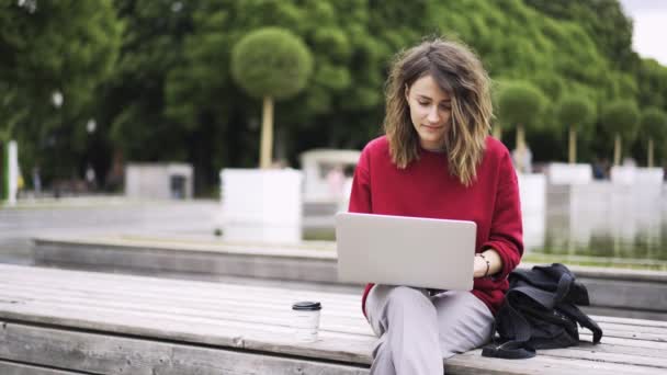 Jonge vrouw dragen rode werken met een laptop in de buurt van een fontein — Stockvideo