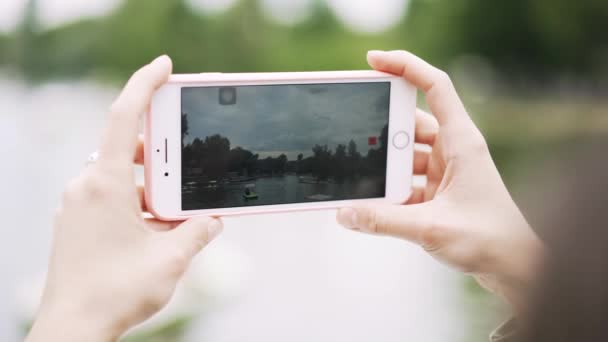 Les mains d'une jeune femme avec un smartphone filmant une vidéo sur la rivière 