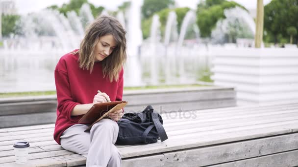 Jonge vrouw in het rood werken met een tablet in de buurt van een fontein — Stockvideo