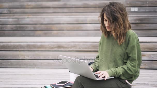 Mujer joven en verde escribiendo en el ordenador portátil fuera — Vídeo de stock