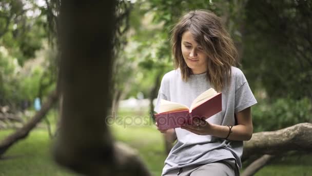 Flicka som läser en bok i en park, panorering skott — Stockvideo