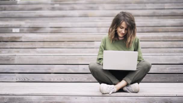 Молодая женщина, сидящая в позе лотоса и печатающая на ноутбуке снаружи — стоковое видео