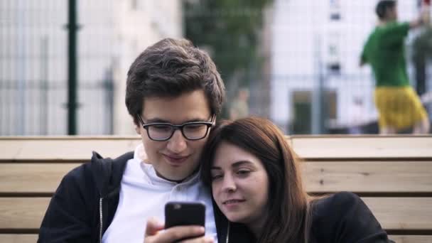 Pareja joven viendo un vídeo en un teléfono inteligente fuera — Vídeos de Stock