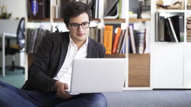 Front view of a young businessman working on a laptop sitting on an office floor — Stock Video