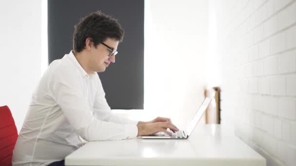 Seitenansicht eines jungen Geschäftsmannes, der in einem weißen Büro auf seiner Laptop-Tastatur tippt — Stockvideo