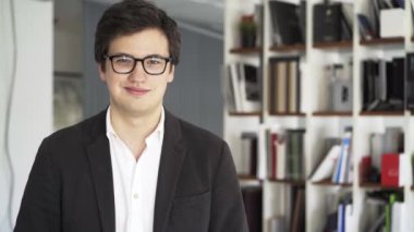 Kameraya bakarak ve gülümseyen bir ofiste gözlüklü genç işadamı