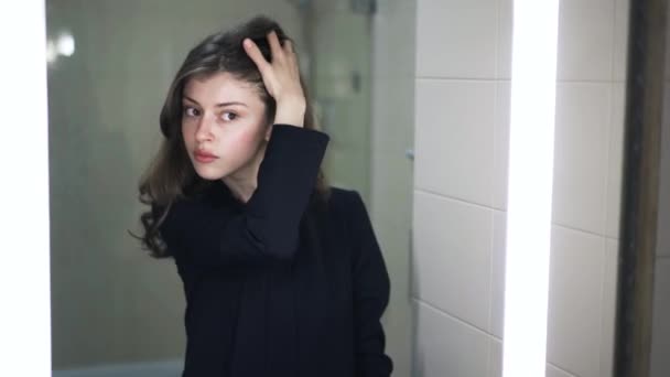 Молода жінка дивиться на себе у дзеркало у ванній — стокове відео