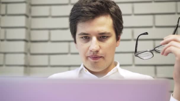 Joven hombre de negocios con gafas trabajando en su portátil en la oficina — Vídeos de Stock