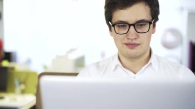 Beyaz gömlekli bir kanepe üstünde laptop üzerinde çalışan genç işadamı