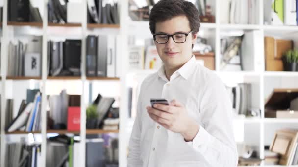 Jovem empresário em óculos de navegação na web com seu smartphone, pan shot — Vídeo de Stock