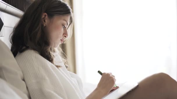Ung kvinna ritning på hennes tablett dator i sängen, sidovy — Stockvideo