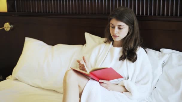 Jonge vrouw leest een boek in bed — Stockvideo