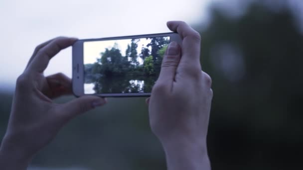 Mujer tomando una foto de un bosque y un lago con su smartphone — Vídeo de stock