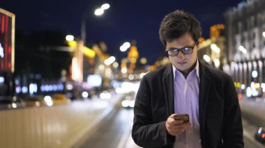 Çekici bir genç işadamı gece şehirde cep telefonunu kullanarak önden görünümü