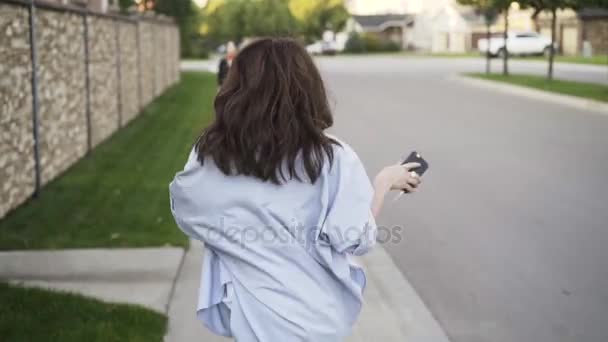 Mujer joven en jeans escuchando la música y bailando en la calle, vista trasera — Vídeos de Stock
