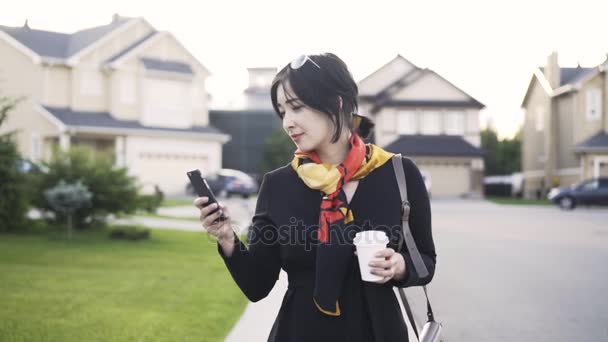 Fröhliche asiatische Frau mit Kaffee schaut auf ihr Handy und geht — Stockvideo