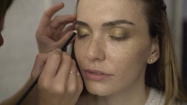 Maquillaje artista aplicando brillantes sombras de oro a hermosos párpados del modelo — Vídeo de stock