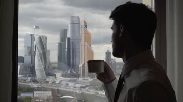 Hombre tomando café mirando las torres de Moscú desde la ventana, día nublado — Vídeos de Stock