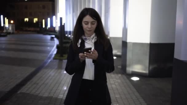 Mujer de negocios caminando por la ciudad nocturna tomando su teléfono inteligente y recibiendo mensajes de Dios — Vídeos de Stock