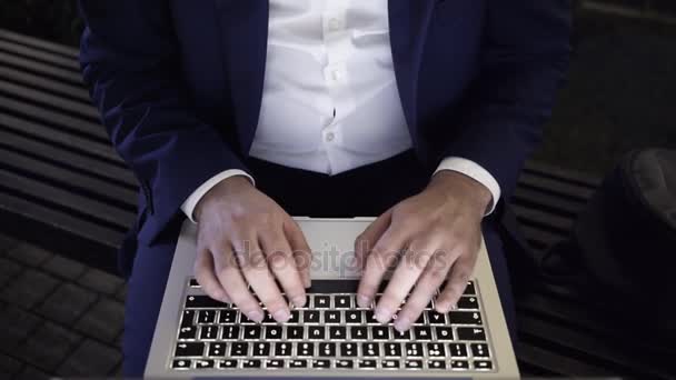 Молодой бизнесмен, работающий с ноутбуком на скамейке в ночное время — стоковое видео