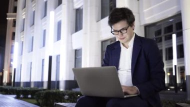 Genç işadamı ile bir dizüstü bilgisayar çalışma gece şehir merkezinde bir bankta