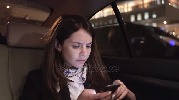 Mujer de negocios frunciendo el ceño mientras mira su teléfono inteligente en un coche — Vídeos de Stock