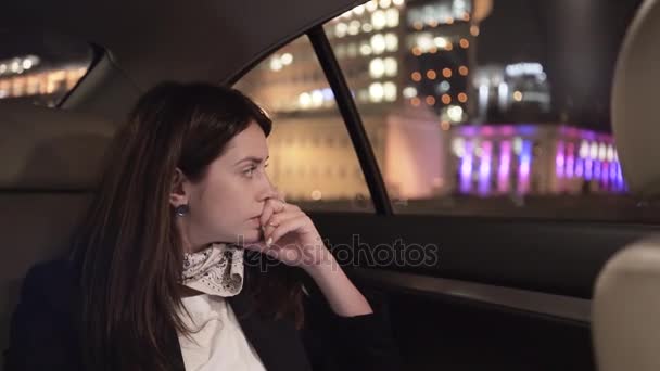 Серьёзная деловая женщина смотрит на ночной город с заднего сиденья своей машины — стоковое видео