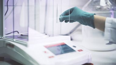 Bilim adamı s elinde bir yeşil eldiven sıvı bir laboratuvarda elektronik ölçeklerde koyuyor. Orta atış