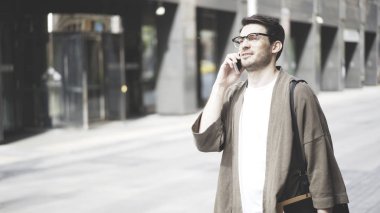 Gözlük ve onun smartphone sokakta konuşurken haki bir ceket giyen bir hipster adam. Portre vurdu