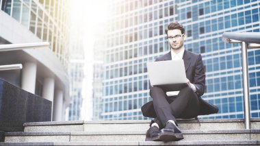 Şehir merkezinde bir dizüstü bilgisayar ile çalışan bir yakışıklı genç iş adamı önden görünümü. Merdiven.