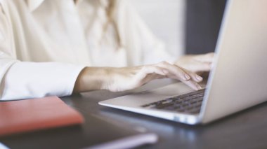 Yazma ve bir ofiste bir dizüstü touchpad kullanarak beyaz bir gömlek giymiş bir kadının yakın çekim.