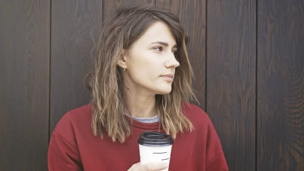 Retrato de una mujer joven con un suéter rojo está bebiendo café . — Foto de Stock