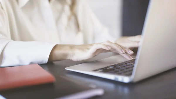 Närbild av en kvinna som bär en vit skjorta att skriva och använda pekplattan på en bärbar dator i ett kontor. — Stockfoto