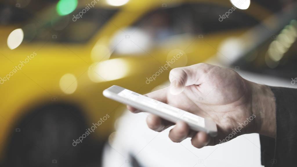 Male hand with smartphone on blurred road background. Taxi service. Night city.