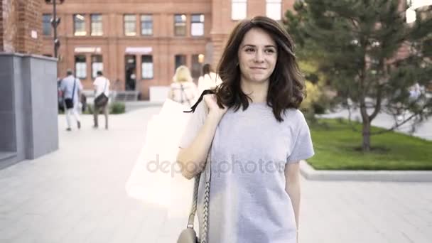Усміхнена темноволоса жінка, що йде від магазину, махає до друга на літній вулиці — стокове відео