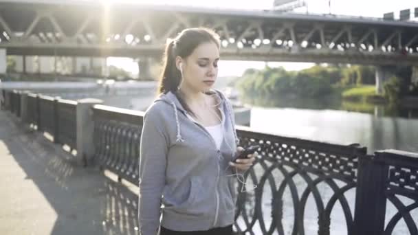 Спокойная брюнетка идет со своим смартфоном вдоль реки Москвы — стоковое видео