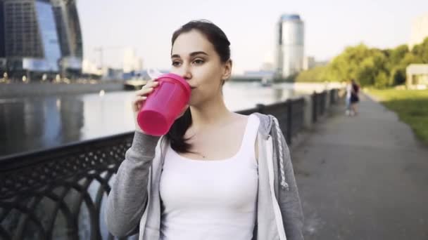 Leende ung kvinna i en sportkläder dricksvatten och promenader i Moskva city — Stockvideo