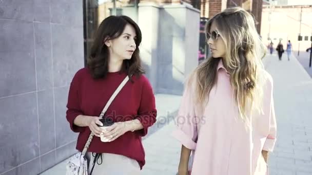 Dos mujeres jóvenes caminando y hablando en una calle de verano con tazas de café — Vídeos de Stock