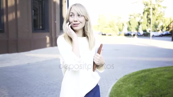 Blonde businesswoman walking in a summer street and talking on her phone — Stock Video