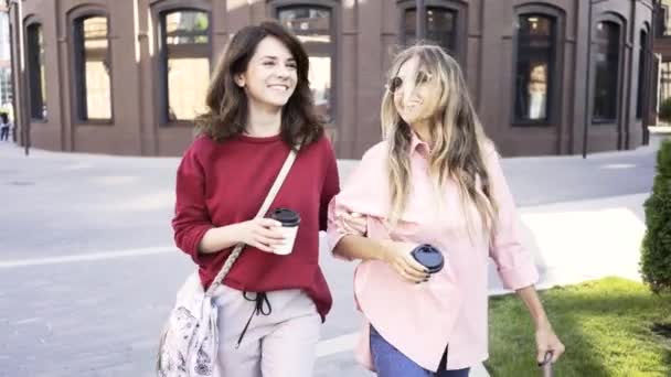 Dos mujeres jóvenes caminando en una calle de verano con tazas de café — Vídeo de stock