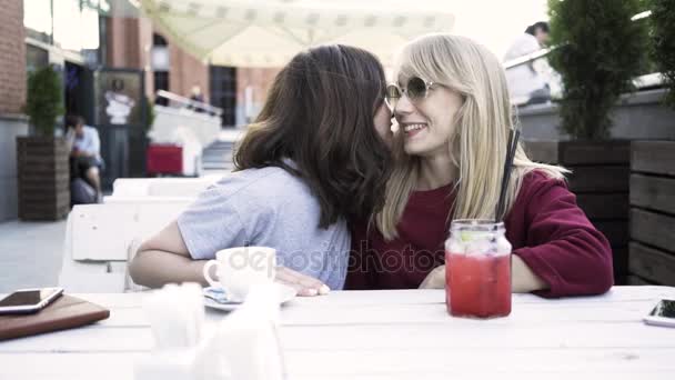 Two girlfriends sharing a secret in an outdoors cafe — Stock Video