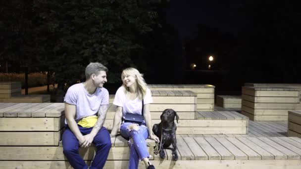 Ungt par kramas och kyssas. Deras hund är dem nära. En natt park — Stockvideo