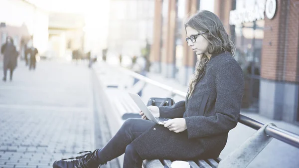 Grave giovane donna in occhiali guardando il suo computer portatile in strada — Foto Stock